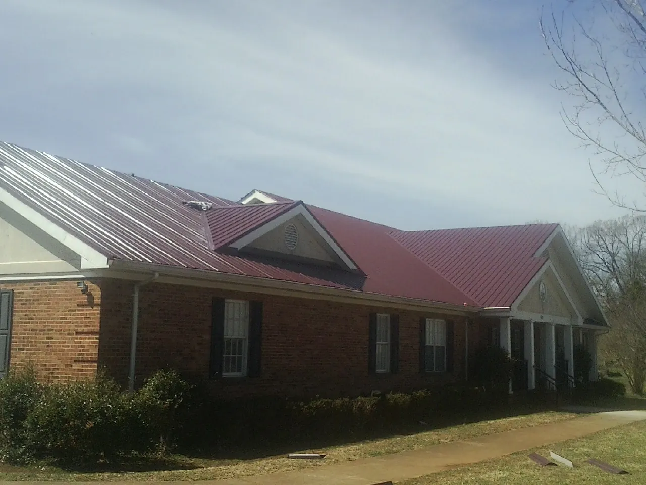 Red metal roof with gabled entries on a long brick building, from a Hail Damage Roof Repair job in Norris