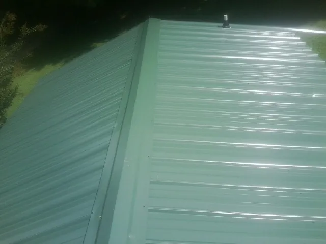 New green metal panels meeting at the ridge of a roof — Flat Roof Repair work by our crew in Norris