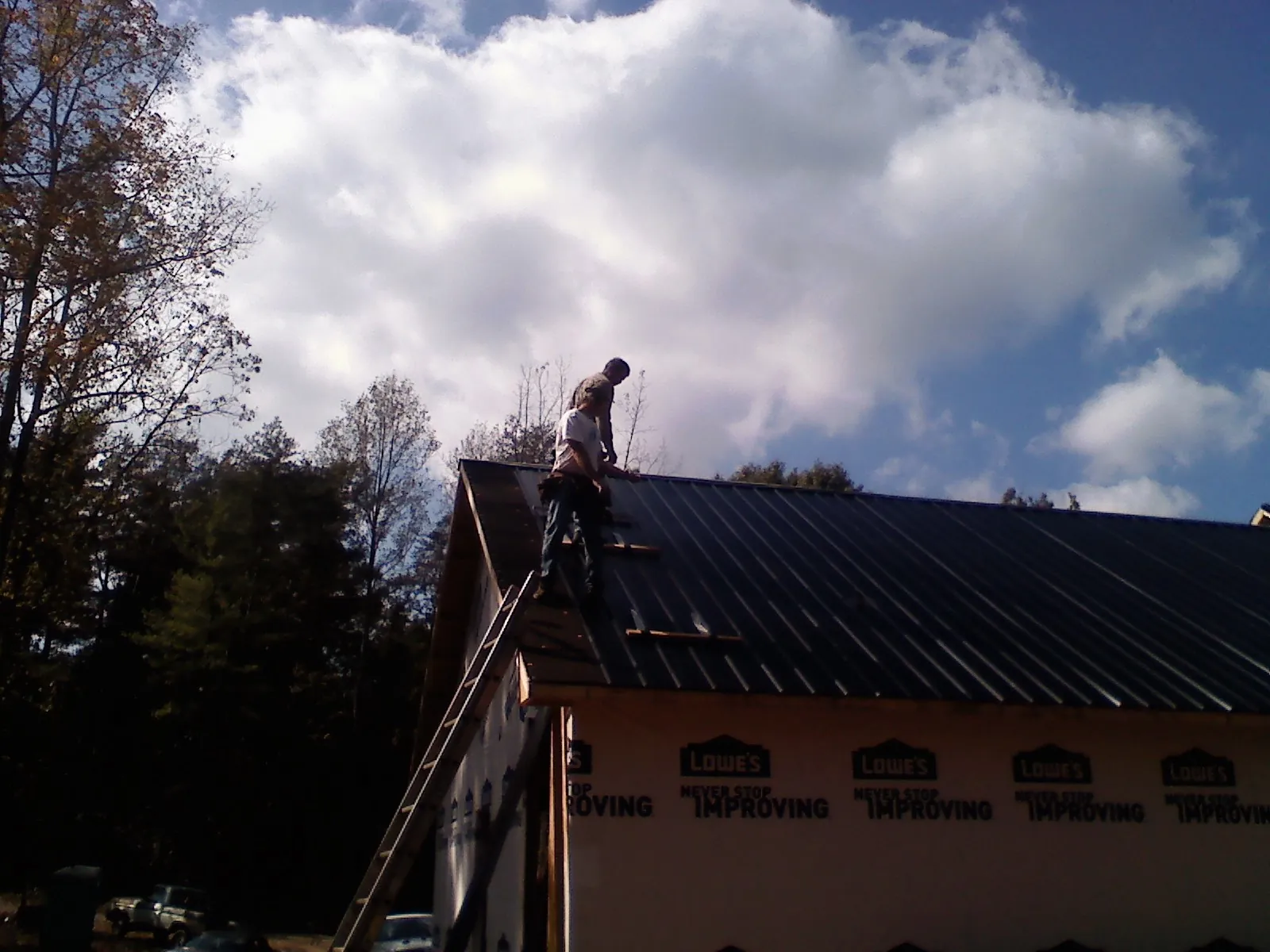 Roofer fastening dark metal panels high against a cloudy sky, from a Roof Inspection job in Norris